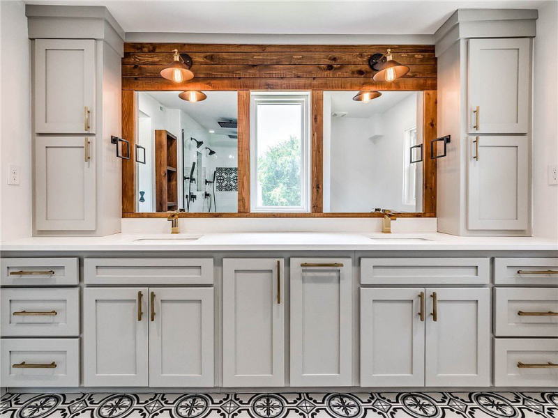 Primary bathroom with double vanity, gold hardware, pattern tile floors, and wood accent wall