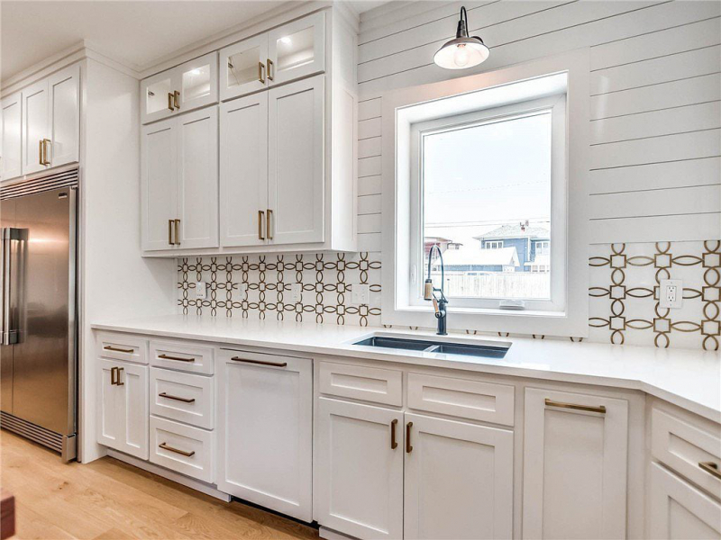 Kitchen sink with white cabinets, gold hardware, shiplap paneled walls, and pattern backsplash