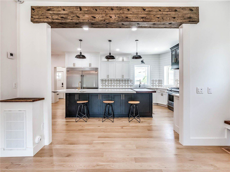 Light and airy kitchen showing oversize island with seating, rustic and farmhouse accents, and wooden header beam