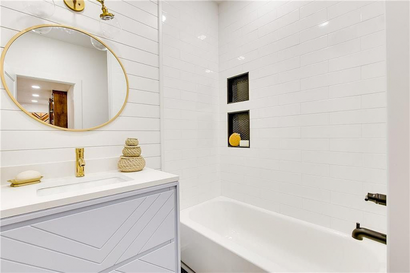 Shower with white subway tile and vanity with white shiplap backsplash and round mirror