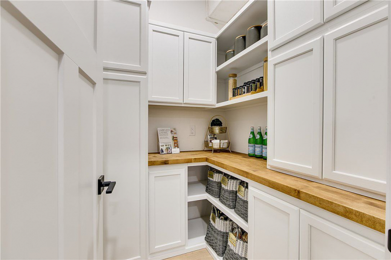 Oversize walk-in pantry with white cabinets and butcher block countertops