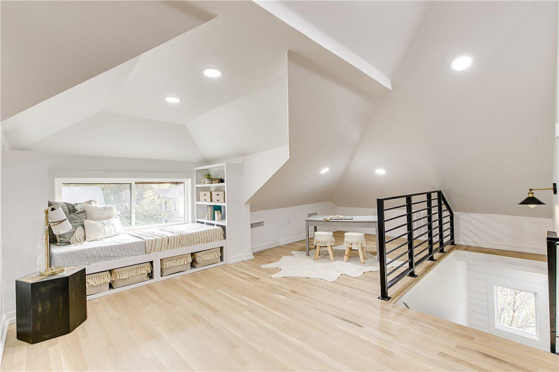 Loft or game room with light wood floors and black metal staircase railing