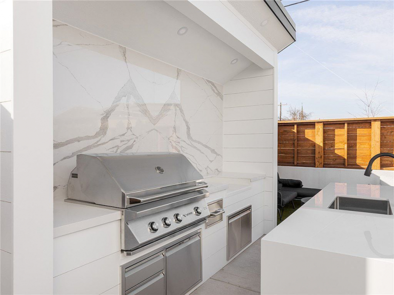 Outdoor built-in gas grill area with white marble backsplash and counters