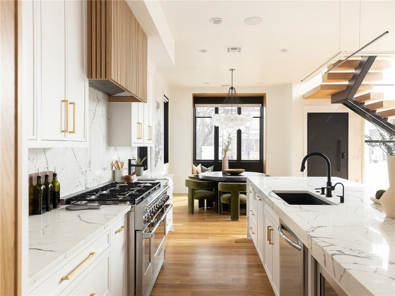 Kitchen with white marble countertops, white cabinets, gold hardware, and wood panel accent